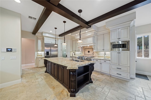 kitchen with tasteful backsplash, built in appliances, beamed ceiling, pendant lighting, and a kitchen island with sink