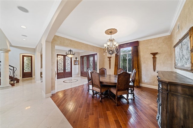 dining space featuring hardwood / wood-style flooring, a notable chandelier, decorative columns, ornamental molding, and french doors