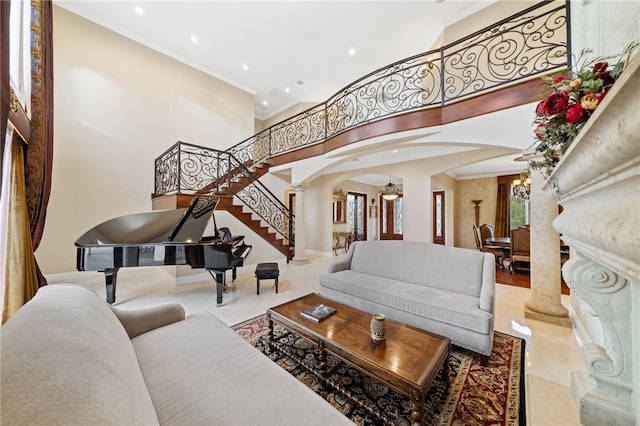 living room featuring crown molding, a towering ceiling, an inviting chandelier, and ornate columns