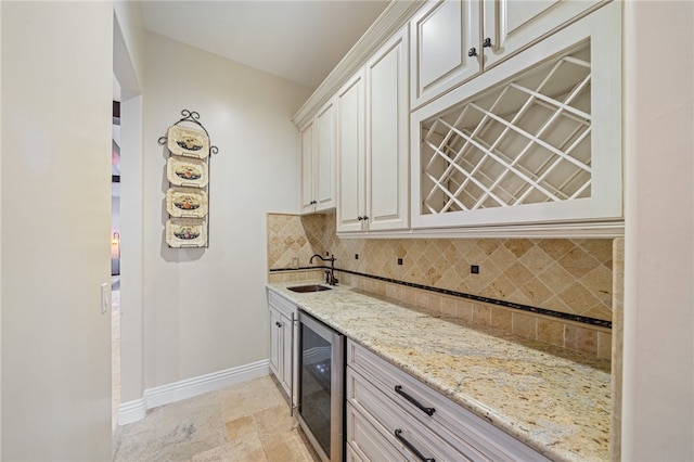 bar with decorative backsplash, white cabinetry, light stone countertops, beverage cooler, and sink