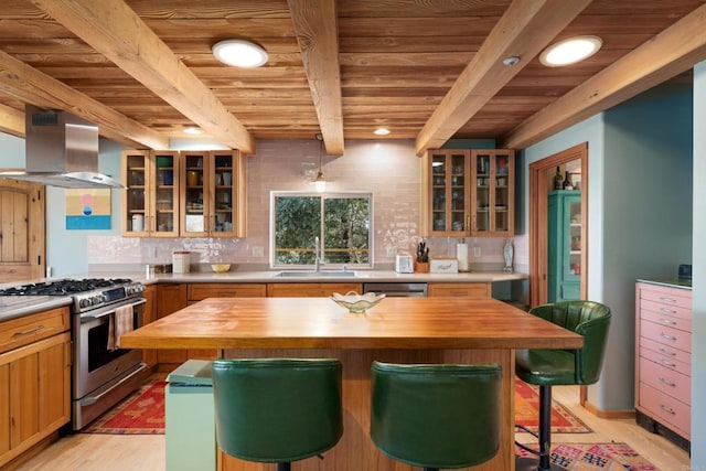 kitchen featuring wall chimney range hood, stainless steel appliances, beamed ceiling, sink, and butcher block countertops