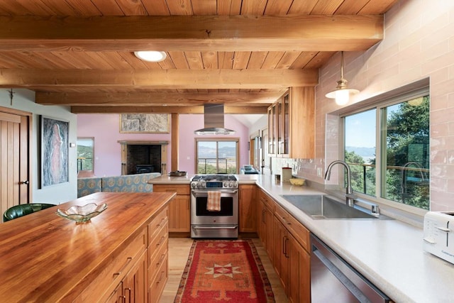 kitchen featuring wall chimney range hood, pendant lighting, butcher block countertops, sink, and stainless steel appliances