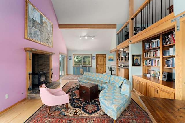 living room featuring a wood stove, light wood-type flooring, track lighting, high vaulted ceiling, and beamed ceiling