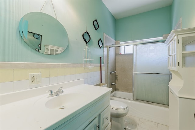 full bathroom featuring tile walls, tile patterned floors, bath / shower combo with glass door, vanity, and toilet