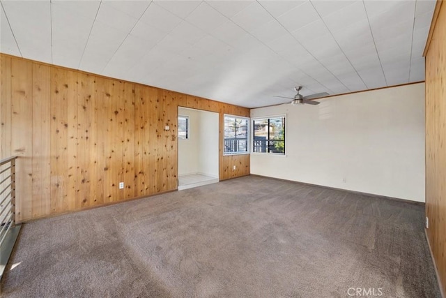 spare room featuring dark carpet, ceiling fan, and wood walls