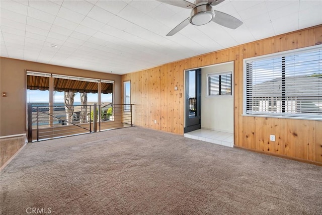 carpeted empty room featuring ceiling fan and wood walls