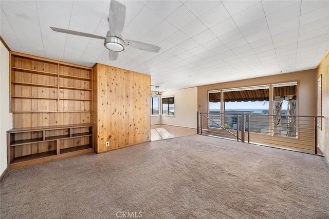 unfurnished living room featuring wood walls, ceiling fan, and carpet flooring