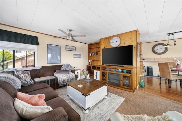 living room with crown molding, carpet floors, wooden walls, and ceiling fan