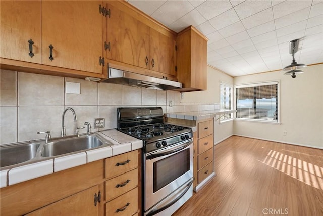 kitchen with stainless steel gas stove, sink, decorative backsplash, and light hardwood / wood-style flooring