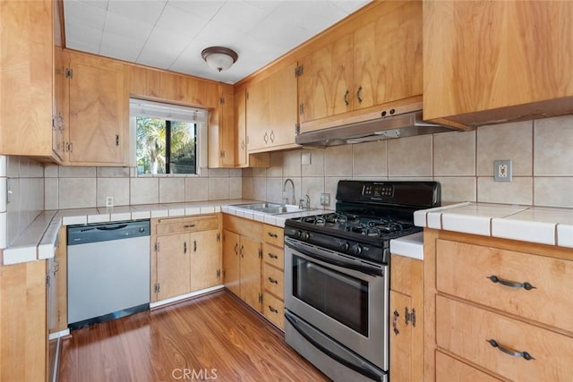 kitchen featuring sink, tile countertops, appliances with stainless steel finishes, hardwood / wood-style floors, and backsplash