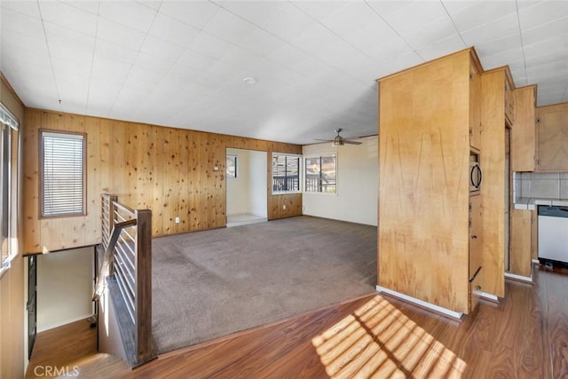 unfurnished room featuring ceiling fan, wooden walls, and dark carpet