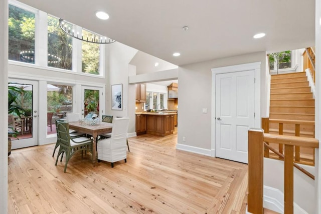 dining room with light hardwood / wood-style flooring, a high ceiling, french doors, and an inviting chandelier