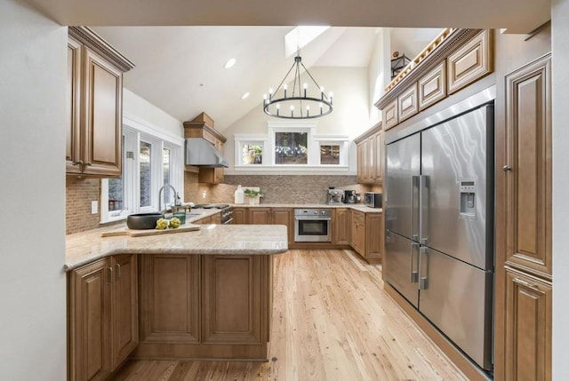 kitchen with stainless steel appliances, an inviting chandelier, kitchen peninsula, lofted ceiling, and decorative backsplash