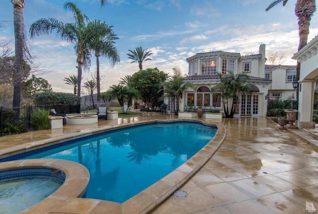 pool at dusk with an in ground hot tub and a patio area