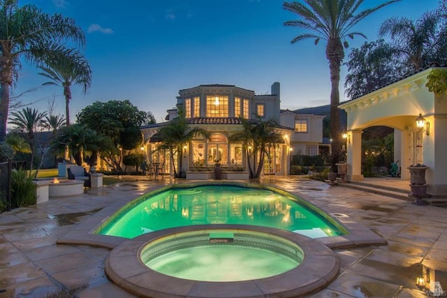 pool at dusk with an in ground hot tub and a patio area