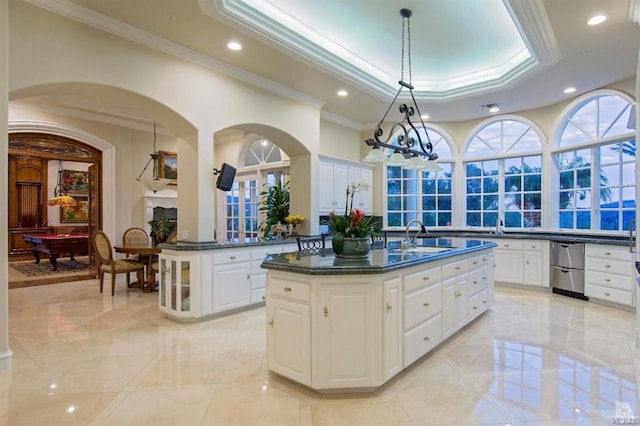 kitchen with decorative light fixtures, a center island with sink, sink, and white cabinetry