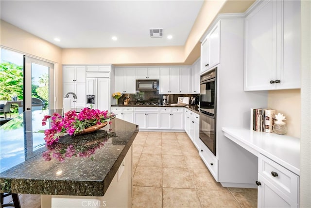 kitchen featuring tasteful backsplash, dark stone countertops, a center island with sink, white cabinets, and black appliances