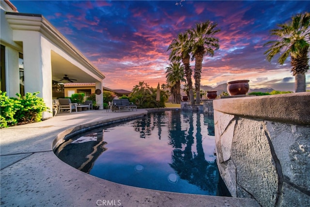 pool at dusk with a patio area and ceiling fan