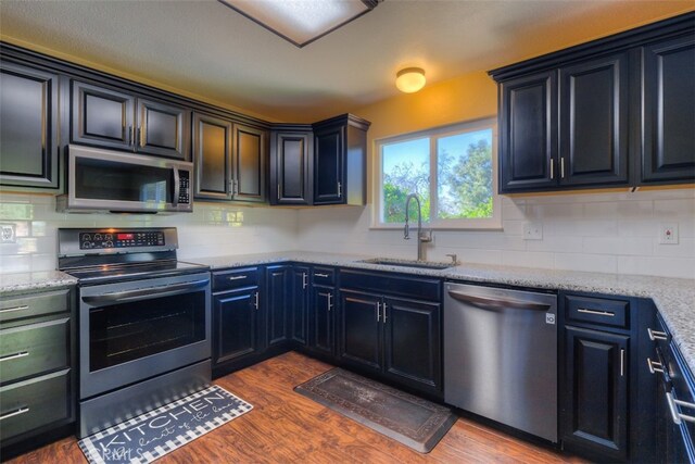 kitchen featuring appliances with stainless steel finishes, decorative backsplash, dark wood-type flooring, light stone counters, and sink