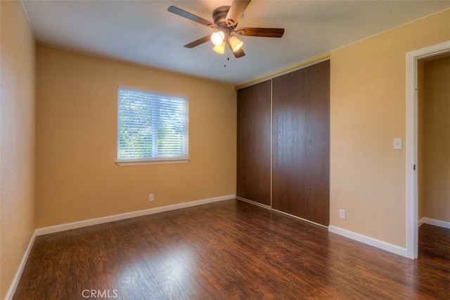 unfurnished bedroom with ceiling fan, a closet, and dark wood-type flooring