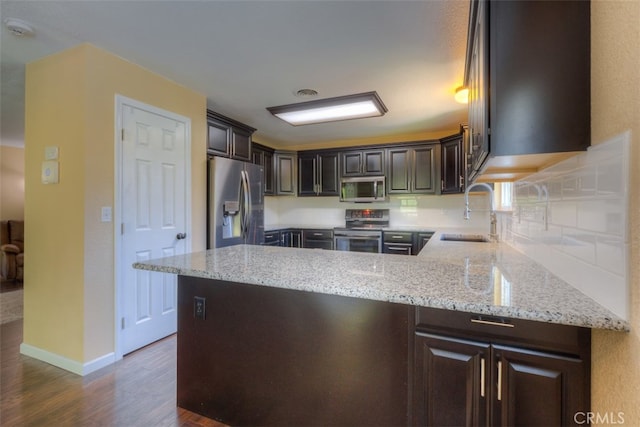 kitchen featuring dark wood-type flooring, light stone counters, stainless steel appliances, dark brown cabinetry, and sink