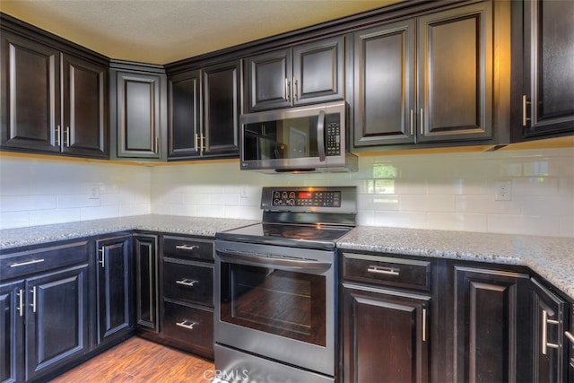 kitchen with light hardwood / wood-style floors, decorative backsplash, stainless steel appliances, dark brown cabinetry, and light stone countertops