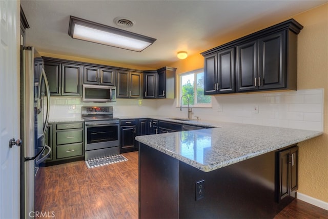 kitchen featuring appliances with stainless steel finishes, kitchen peninsula, sink, and light stone counters