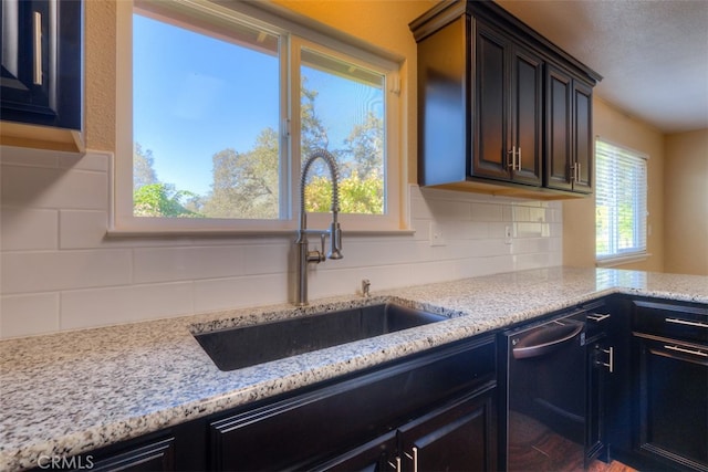 kitchen featuring dishwasher, light stone counters, tasteful backsplash, and sink