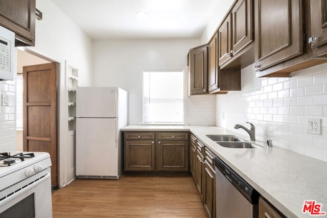 kitchen featuring light wood-type flooring, backsplash, white appliances, and sink