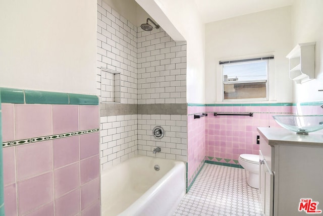 full bathroom with tiled shower / bath, vanity, tile patterned floors, tile walls, and toilet