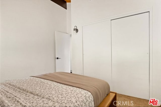 bedroom with carpet floors, beamed ceiling, and a closet