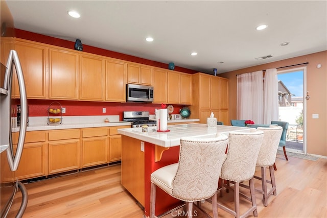 kitchen featuring light hardwood / wood-style floors, a kitchen island, a kitchen breakfast bar, stainless steel appliances, and tile countertops