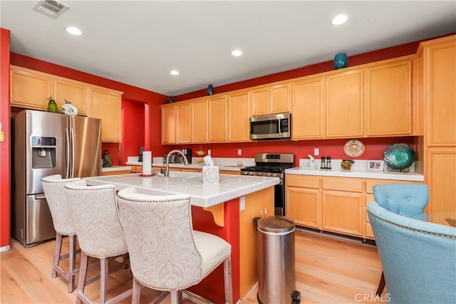 kitchen with stainless steel appliances, light hardwood / wood-style floors, a kitchen island with sink, and a breakfast bar area