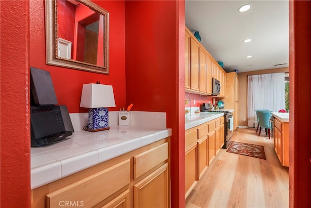 kitchen featuring tile countertops, appliances with stainless steel finishes, and light wood-type flooring