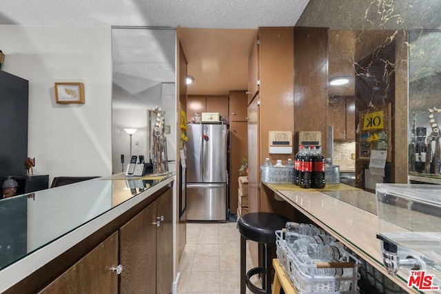 kitchen with backsplash, a textured ceiling, stainless steel fridge, and light tile patterned floors