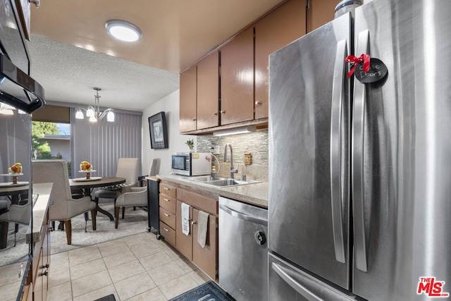 kitchen featuring appliances with stainless steel finishes, backsplash, pendant lighting, sink, and a chandelier