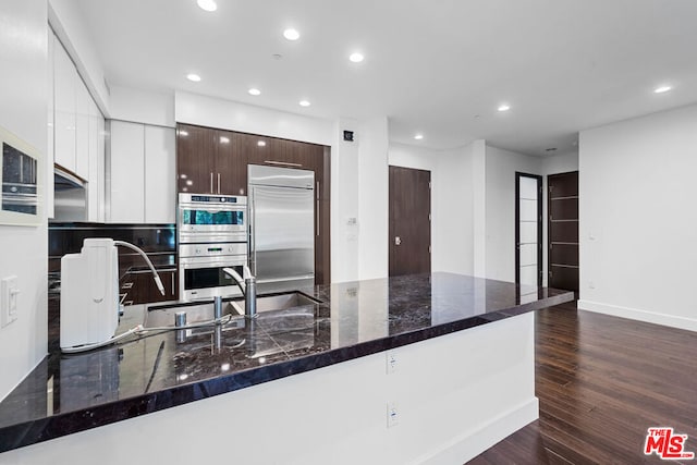 kitchen featuring dark hardwood / wood-style flooring, dark brown cabinetry, stainless steel appliances, dark stone countertops, and white cabinetry