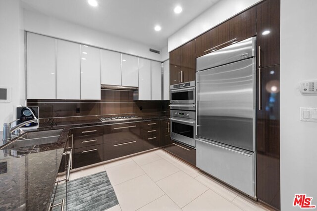 kitchen with white cabinetry, sink, dark stone counters, light tile patterned floors, and appliances with stainless steel finishes