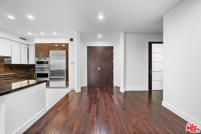 kitchen with appliances with stainless steel finishes, dark hardwood / wood-style flooring, white cabinetry, and dark stone counters