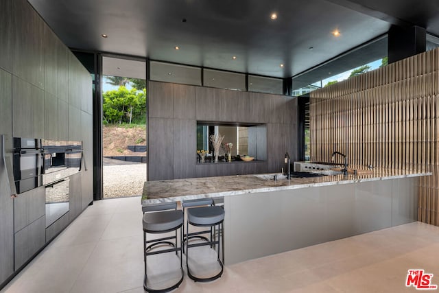 kitchen featuring a kitchen bar, kitchen peninsula, light stone counters, and sink