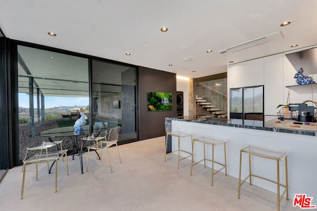 kitchen with a kitchen breakfast bar, white cabinetry, stainless steel refrigerator, and dark stone countertops