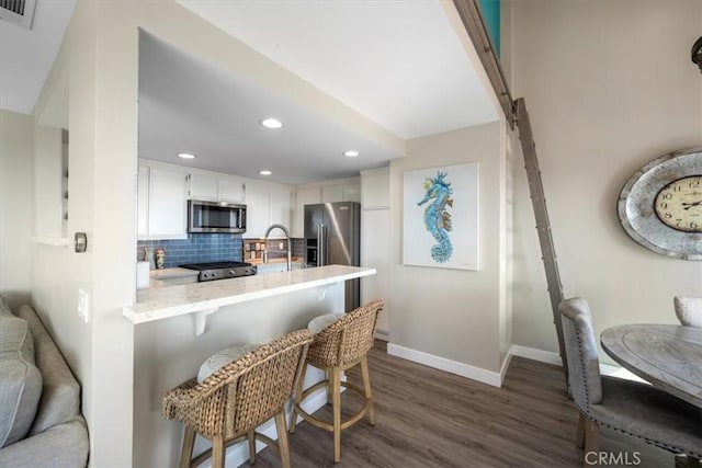 kitchen featuring kitchen peninsula, backsplash, stainless steel appliances, white cabinets, and a breakfast bar area