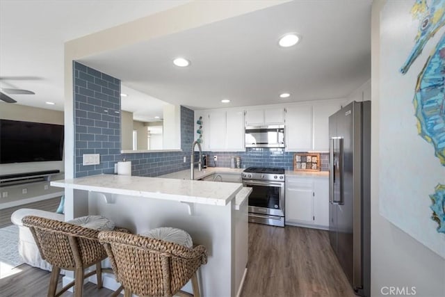 kitchen featuring backsplash, kitchen peninsula, appliances with stainless steel finishes, white cabinetry, and a breakfast bar area