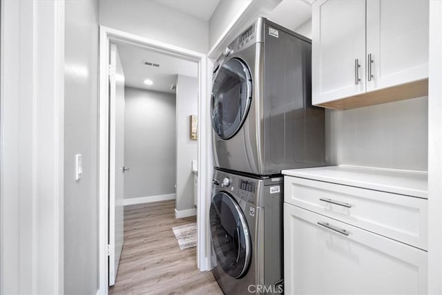 clothes washing area with stacked washer / dryer, light hardwood / wood-style flooring, and cabinets