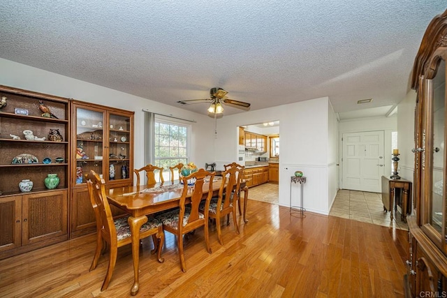 dining area with ceiling fan, light hardwood / wood-style flooring, and a textured ceiling