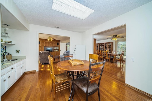 dining area featuring a skylight, ceiling fan, sink, and light hardwood / wood-style floors