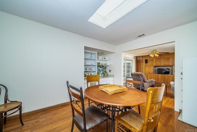 dining space featuring a skylight, ceiling fan, a textured ceiling, and hardwood / wood-style flooring