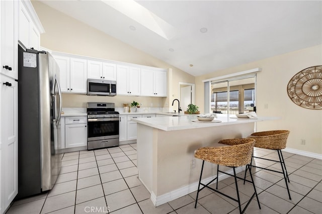 kitchen with lofted ceiling, a kitchen bar, white cabinetry, light tile patterned floors, and appliances with stainless steel finishes