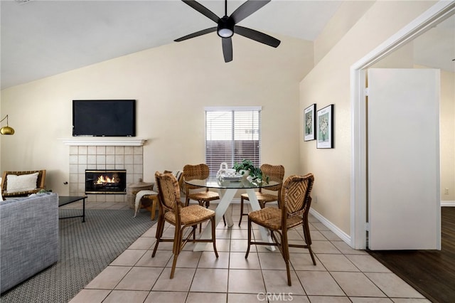 dining space featuring light hardwood / wood-style floors, high vaulted ceiling, a tile fireplace, and ceiling fan