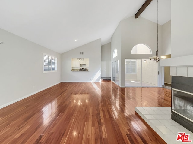 unfurnished living room with light hardwood / wood-style floors, high vaulted ceiling, a fireplace, beamed ceiling, and a notable chandelier